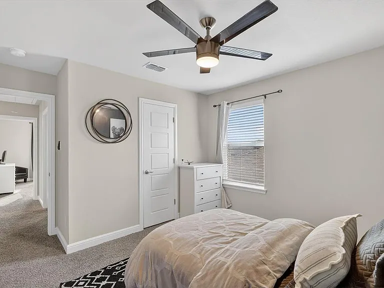 Carpeted bedroom featuring a bronze-finish ceiling fan with integrated lighting, a four-panel interior door, and a window with blinds