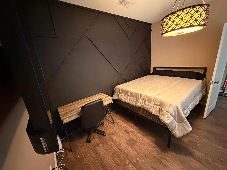 Furnished bedroom with a queen bed, dedicated work desk, and statement accent wall with overhead pendant lighting.