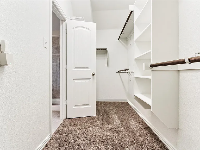 Walk-in closet featuring white built-in shelving, wood-finish hanging rods, and brown carpet flooring