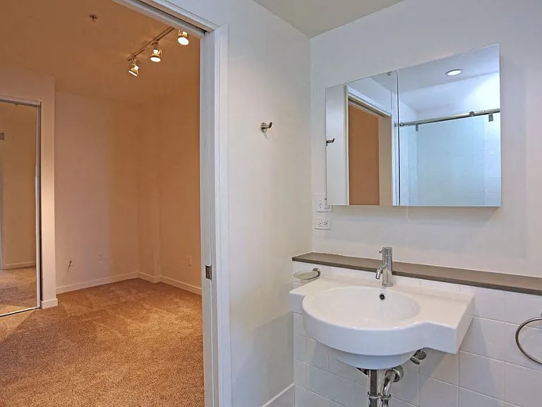 Bathroom and carpeted bedroom with large mirrored door closets at 12th Street Lofts in National City, California.