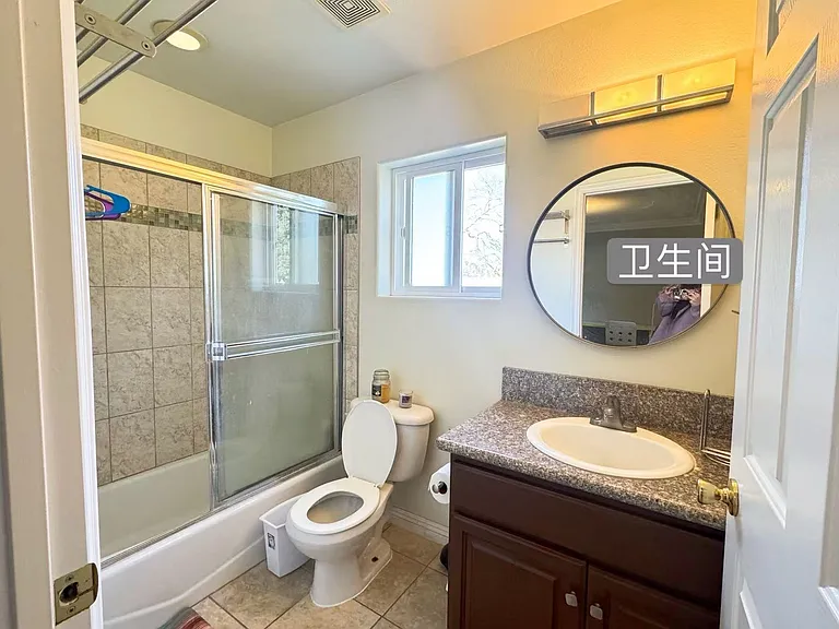 Private full bathroom servicing the second bedroom, detailed with a modern round mirror, granite-look countertops, and a tiled shower.