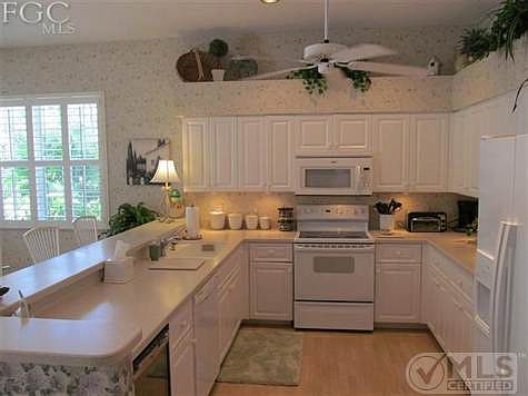 Large kitchen with upgraded white cabinets, plant shelf, side by side refrigerator, and laminate floors.
