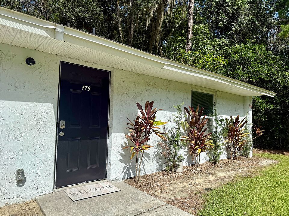 Charming home entrance featuring a dark door framed by lush greenery and vibrant plants, inviting atmosphere with a welcoming doormat.