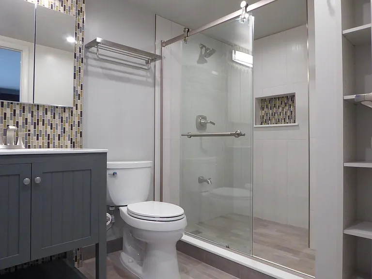 Bright bath with designer fixtures, stylish tiles, step-in shower with trendy glass doors, and built-in shelving.