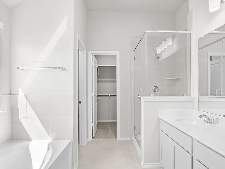 Spa-like primary bath with soaking tub, separate glass-enclosed shower, double vanity, and direct access to the walk-in closet.