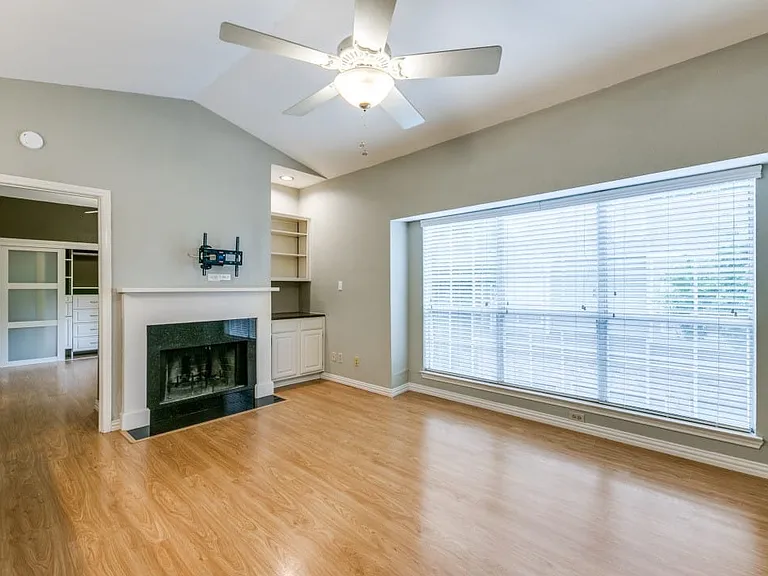 Living room with ceiling fan, lofted ceiling, a premium fireplace, and light hardwood / wood-style flooring.