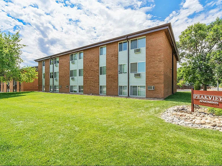 Charming Peakview Apartments exterior showcasing a beautifully maintained lawn, lush trees, and a welcoming atmosphere under a bright blue sky.