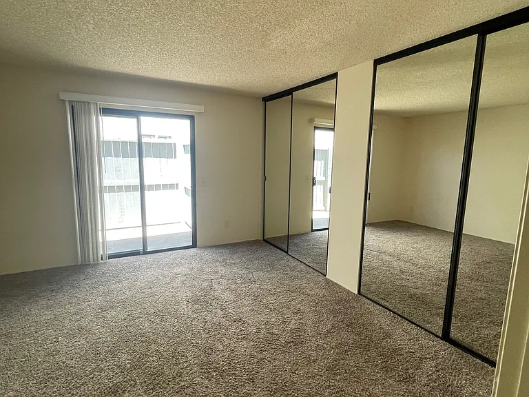 Bedroom has two mirrored closet doors and a small patio