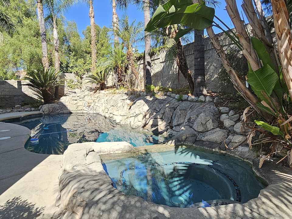 Backyard rock pool and spa - an oasis surrounded by flowers, palm trees, and pine trees