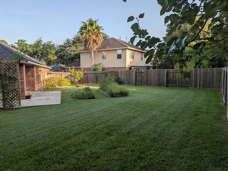 Another angle showing the brick back patio and the generous lawn space bordered by mature trees.
