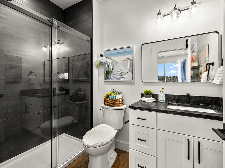 Stylish en-suite bath with a sleek glass-enclosed shower, granite countertops, and modern black finishes, offering a clean and refined feel for the bedroom suite.