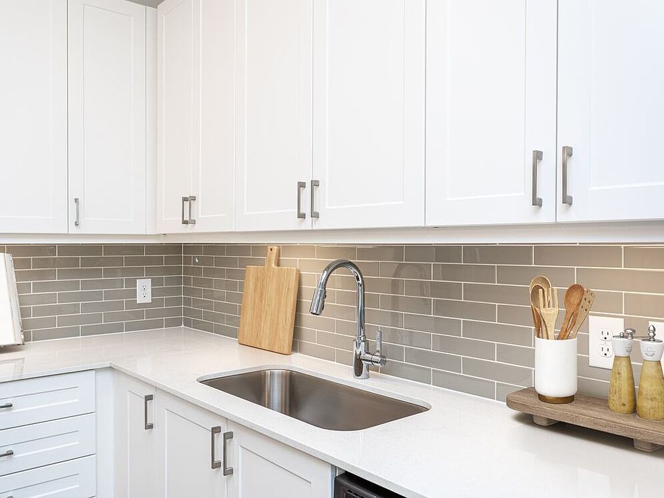 Kitchen with white cabinetry, grey tile backsplash, white quartz countertops, and undercabinet lighting