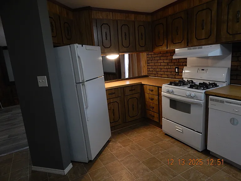 kitchen -showing refrigerator/freezer - cooking range with vent hood -dish washer at right - lighted counter top at rear of photo-