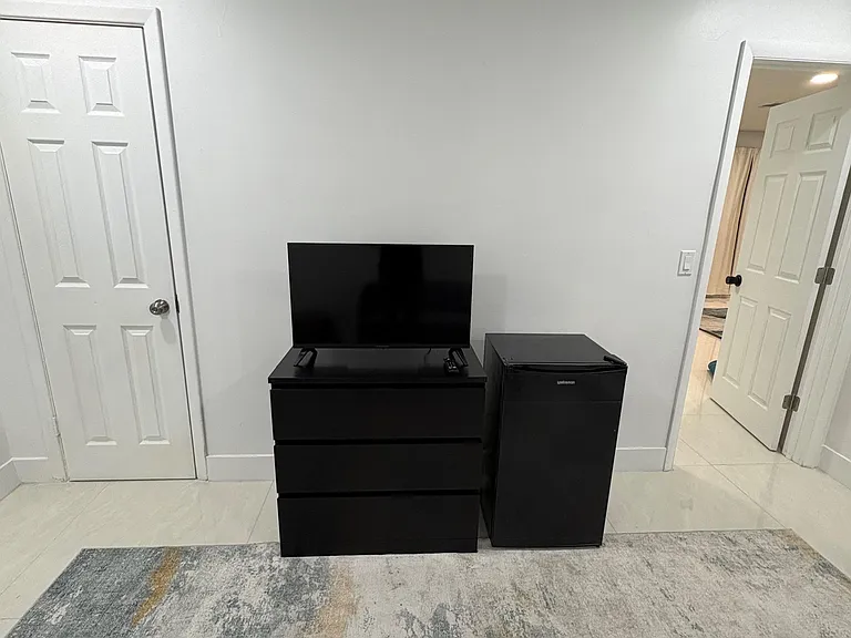 Private room featuring tile flooring, a dresser with TV, and an in-room mini fridge, with easy access to nearby hallways.