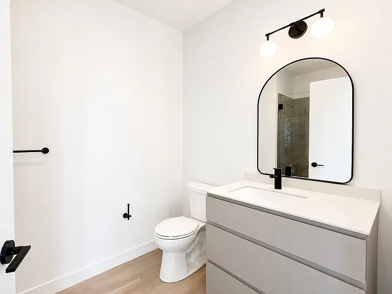 Full bathroom at Stead 220 in Fulton Market, featuring a modern white vanity, an arched mirror, matte black fixtures, and a glass-enclosed walk-in shower with designer tile.
