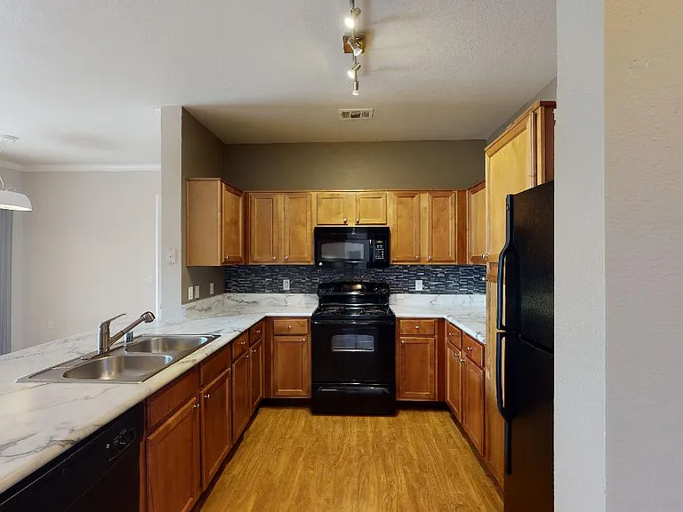 Apartment kitchen with marble-style countertops and wood-style flooring.