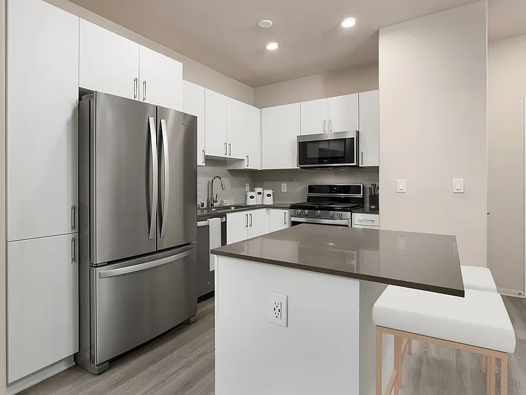 Renovated Package I kitchen with quartz countertops, white cabinetry, stainless steel appliances, hard surface vinyl plank flooring, and tile backsplash