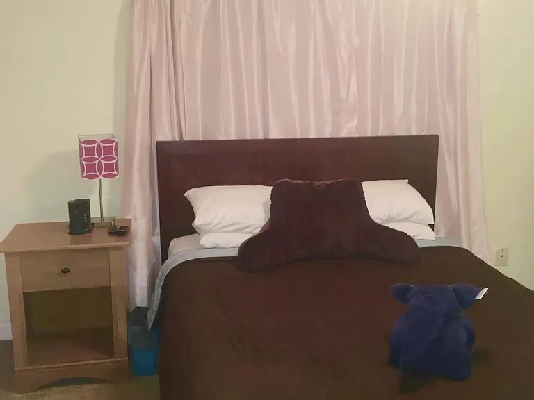 Furnished bedroom featuring a full-size bed, bedside table with lamp, and window dressed with curtains for added privacy.