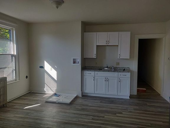Portion of the kitchen showing brand new luxury plank flooring (installed throughout the unit), real wood cabinets, and in unit laundry hookup (with overflow pan).