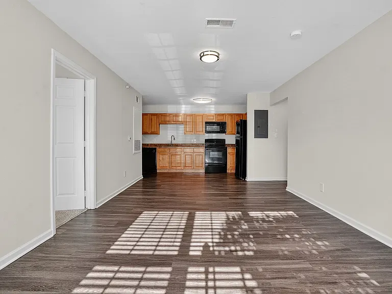 Modern open-concept living space with wood floors and a sleek kitchen featuring wooden cabinets and black appliances.