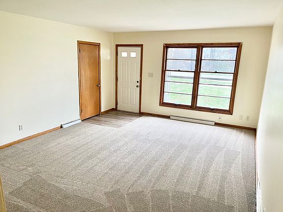 Large living room with new carpet, big windows and coat closet at the entrance.