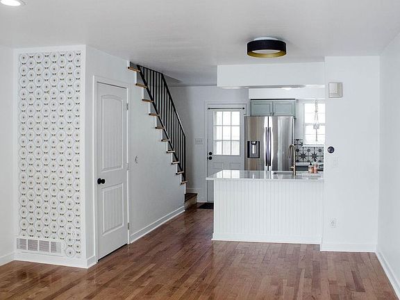 Open living room with area for small dining nook and barstools. Door to pantry under stairs.