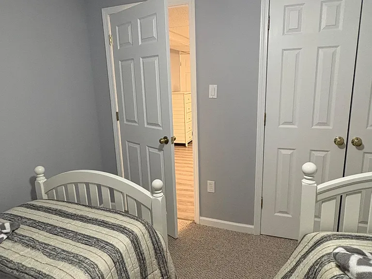 Carpeted bedroom with two twin beds, neutral walls, and a closet for convenient storage with easy hall access.
