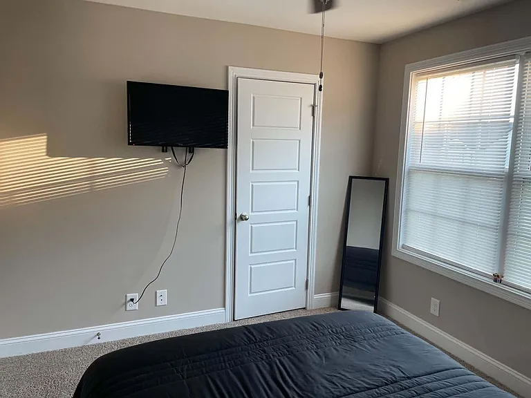 Bedroom with carpeted floors, a large window with blinds, and a wall-mounted TV for convenient in-room entertainment.