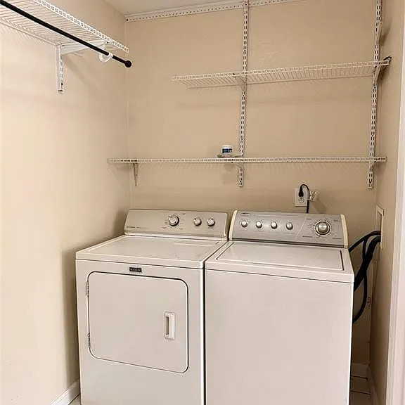 Laundry area featuring white tile flooring, wall-mounted wire shelving, and a hanging rod
