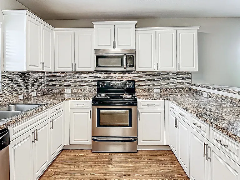 Our kitchens feature stainless steel appliances, elegant white cabinetry, and granite-style countertops with a stylish backsplash, providing both functionality and luxury.