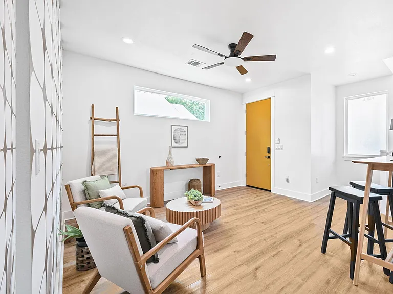Open living area with seating nook, ceiling fan, wide-plank floors, and adjacent dining space near the entry.