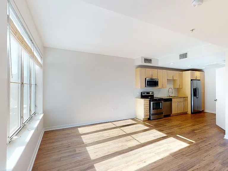 Apartment kitchen with stainless steel appliances, dining and living room with wood-style flooring.