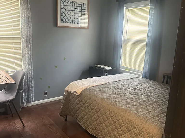 Private bedroom with hardwood floors, two windows with blinds, and a ceiling fan for year-round comfort.