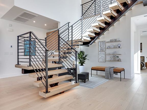 A modern, open-concept interior with a sleek, metal staircase leading up to a second level, surround