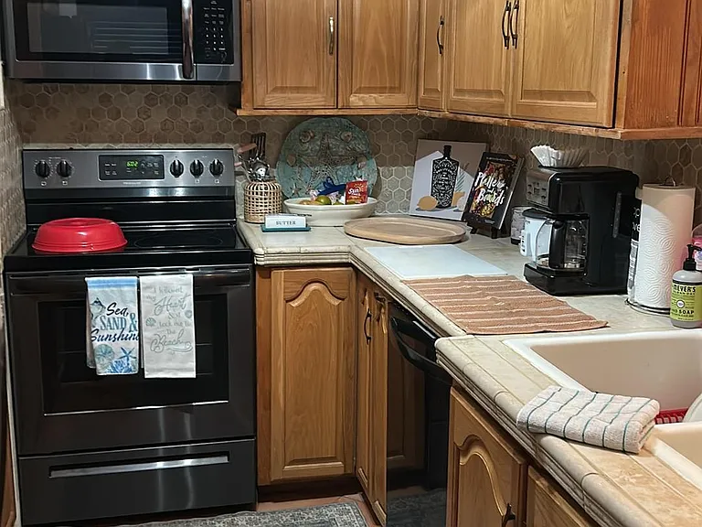 U-shaped kitchen with ample wood cabinetry, tile flooring, and stainless range with over-the-range microwave plus double sink