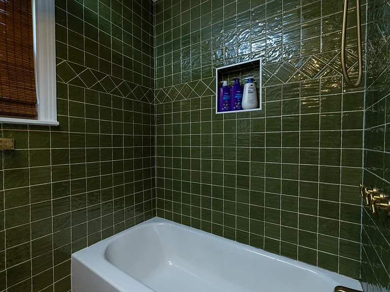 Stylish bathroom with rich green tile, gold accents, and a modern vanity. Enjoy a relaxing soak in the deep tub surrounded by elegant finishes _ a spa-like retreat with timeless charm.