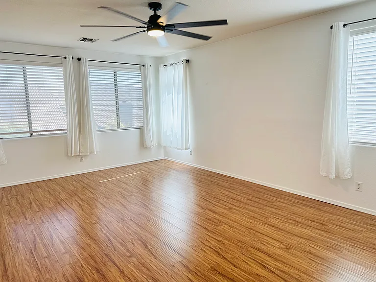 Spacious primary bedroom with abundant natural light from multiple windows, wood-look flooring, and an updated ceiling fan.