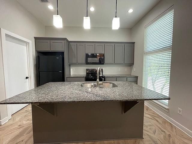 Kitchen featuring gray cabinetry, dark stone countertops, a center island with sink, black appliances, and recessed lighting
