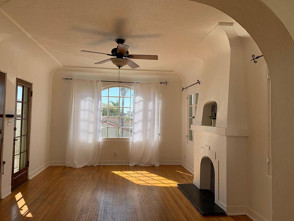 Sun filled living room with coved ceiling, original hardwood floors and faux fireplace.