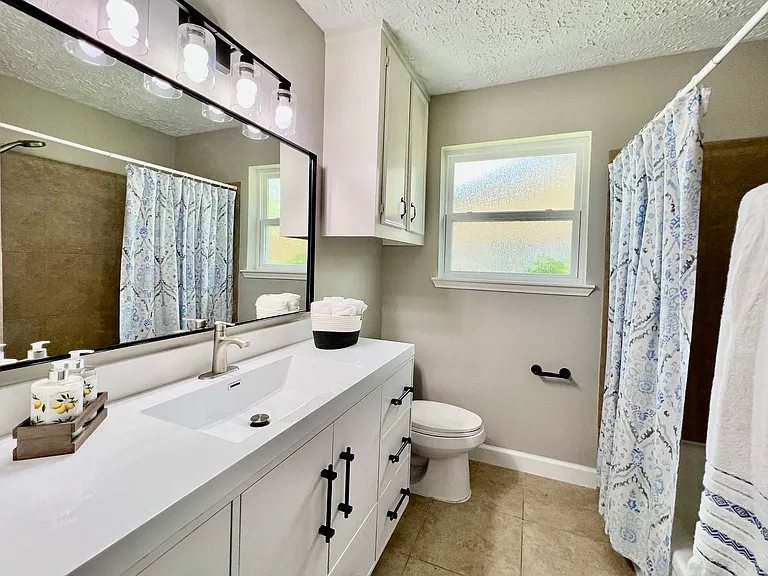 Remodeled main bathroom with a sleek modern vanity, stylish mirror & light fixture, and fresh paint offers a clean and elegant feel.