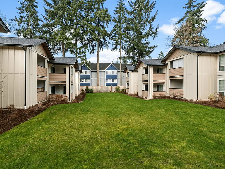 Open landscaped courtyard at Boardwalk at University Place surrounded by renovated apartment homes and tall evergreen trees.