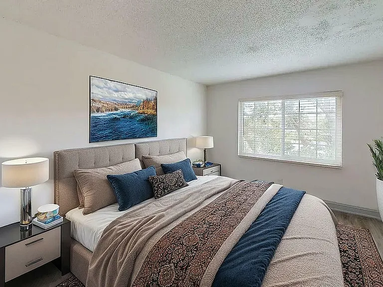 Bright and cozy bedroom with elegant decor, featuring a plush king-sized bed, stylish side tables with lamps, large window for natural light, and serene artwork.