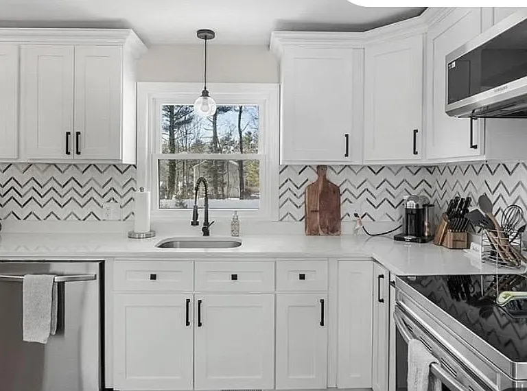 Spacious kitchen with ample white cabinetry, full-size stainless appliances, and a large counter workspace under a window.