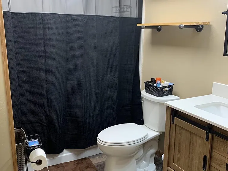 Full bathroom with tub/shower combo, vanity with countertop sink, and open wall shelving for added storage.
