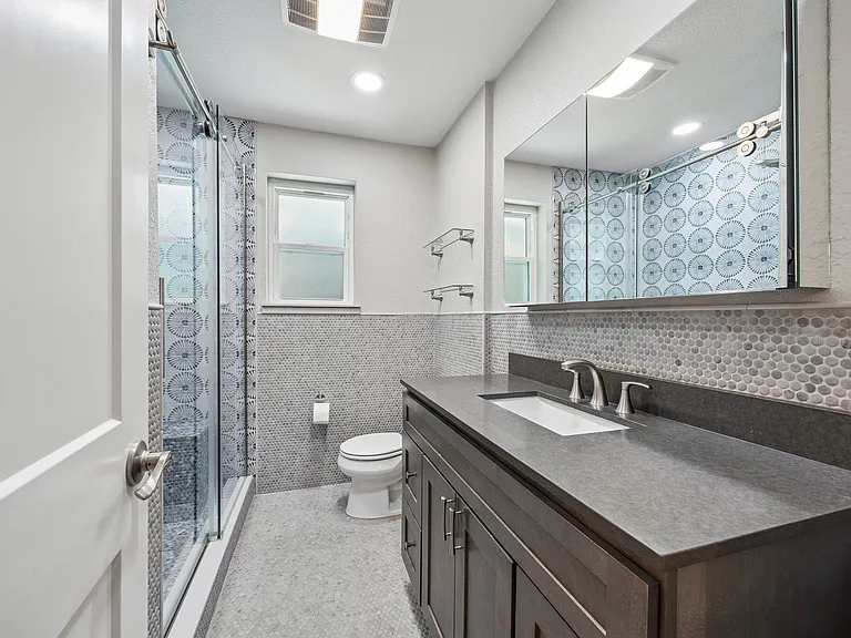 Bathroom featuring a dark wood-finish vanity with an integrated sink, a large mirrored medicine cabinet, and a glass-enclosed shower with a barn door style entry