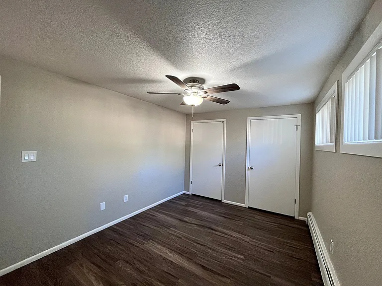 Bright and inviting room with elegant wood flooring, featuring a ceiling fan and ample natural light from modern windows.