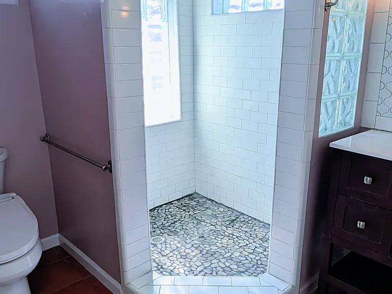 Walk=in shower with rainhead, smooth pebble floor, and privacy glass brick for light.