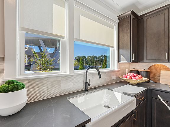 A modern kitchen with a large window overlooking a lush outdoor landscape, featuring a farmhouse-sty