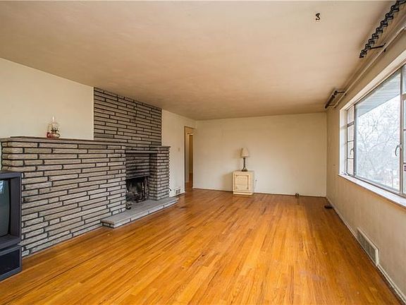 The carpet in the living room has been pulled to exposed the wood floors.  The log burning fireplace with stone surround is the 