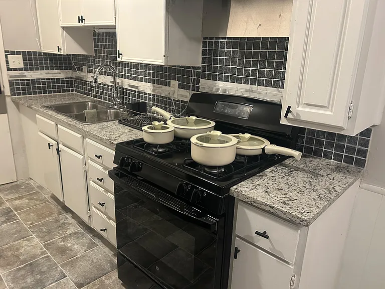 Efficient galley kitchen with ample cabinet storage, tiled backsplash, double-basin sink, and full-size range.